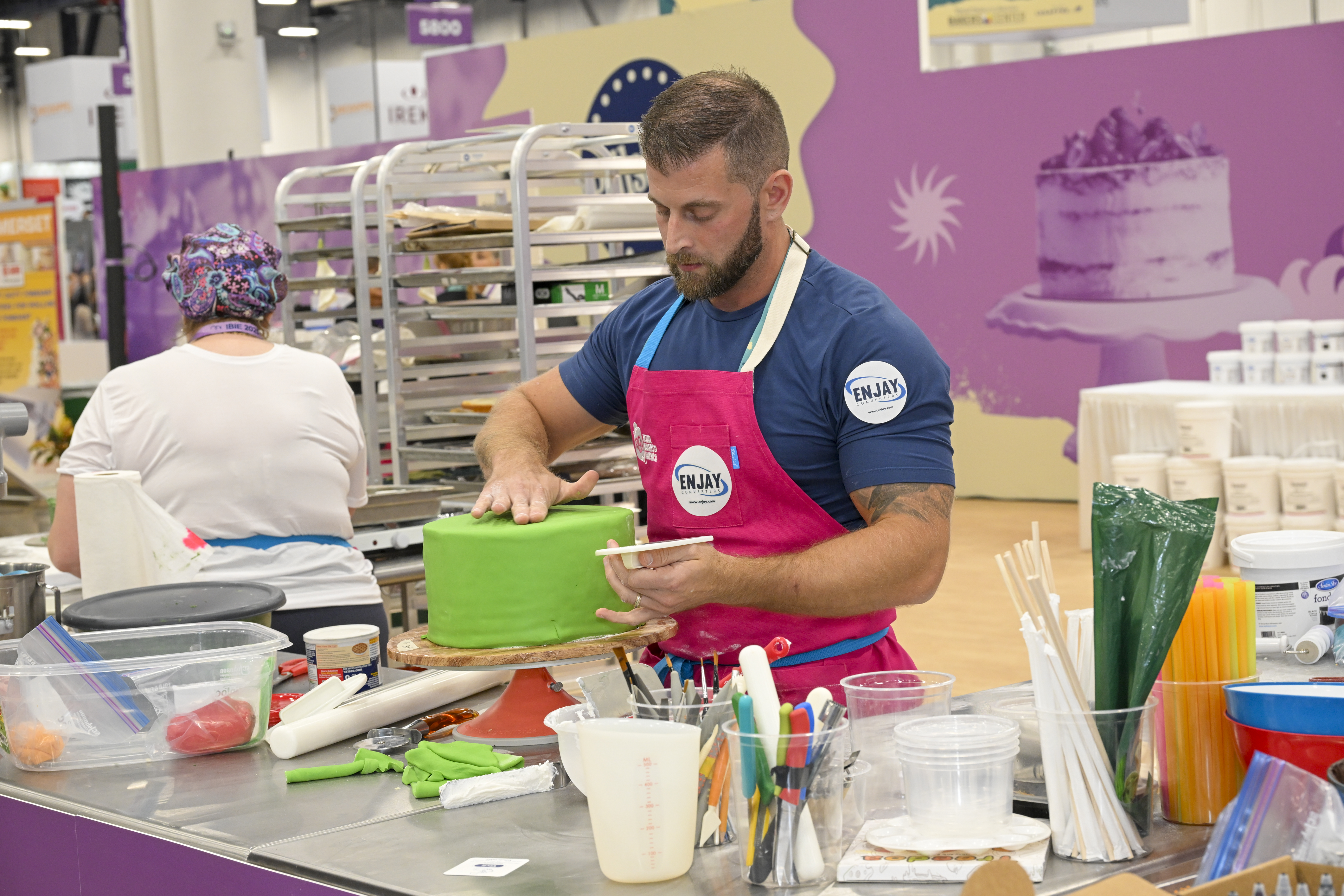 Man in apron decorating a cake with green frosting